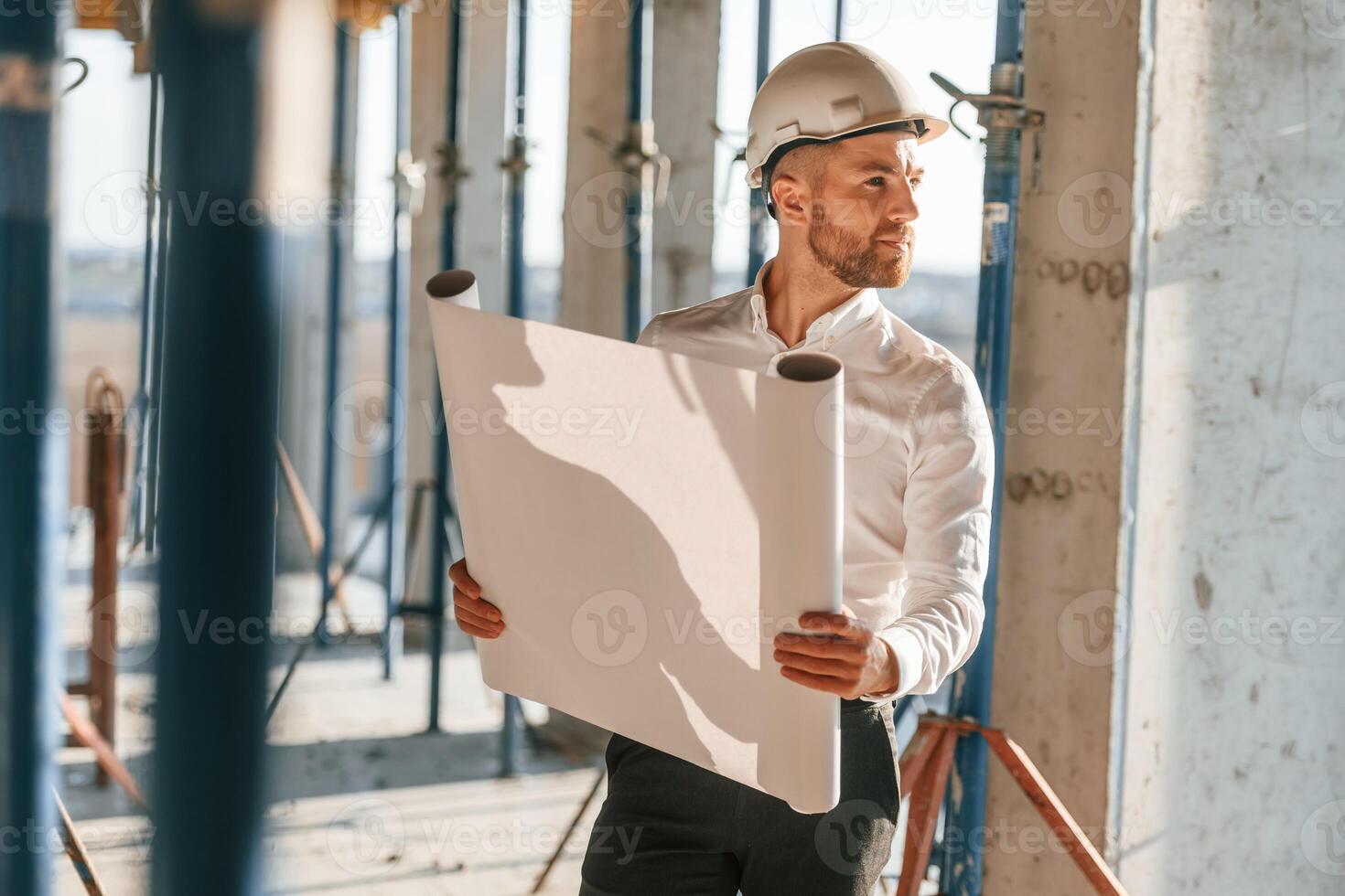 With big paper in hands. Man is working on the construction site at daytime photo