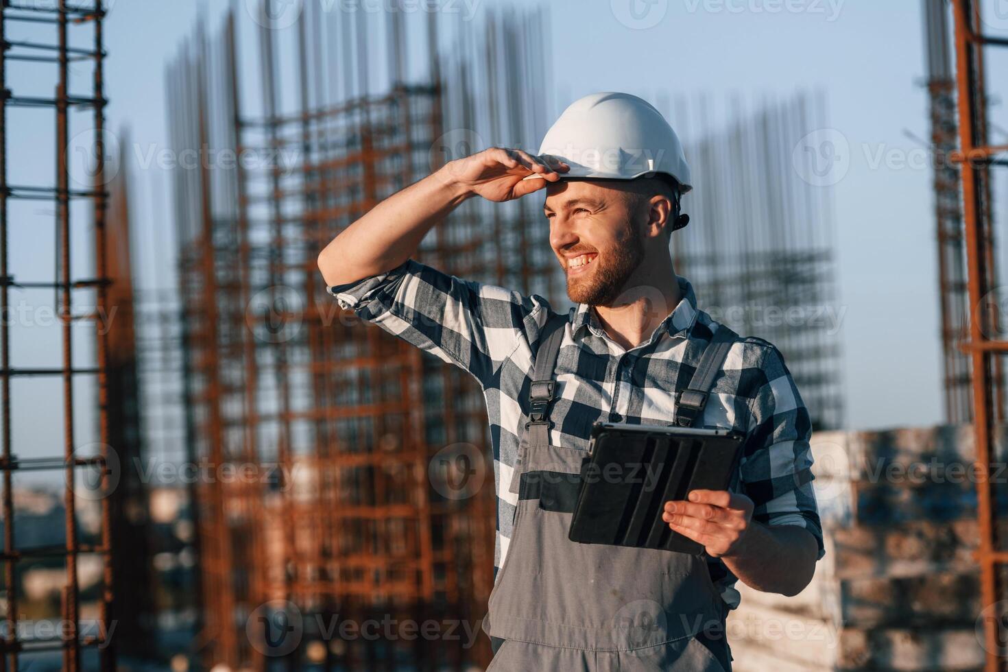 Looking to the side. Holding ,tablet. Man is working on the construction site at daytime photo