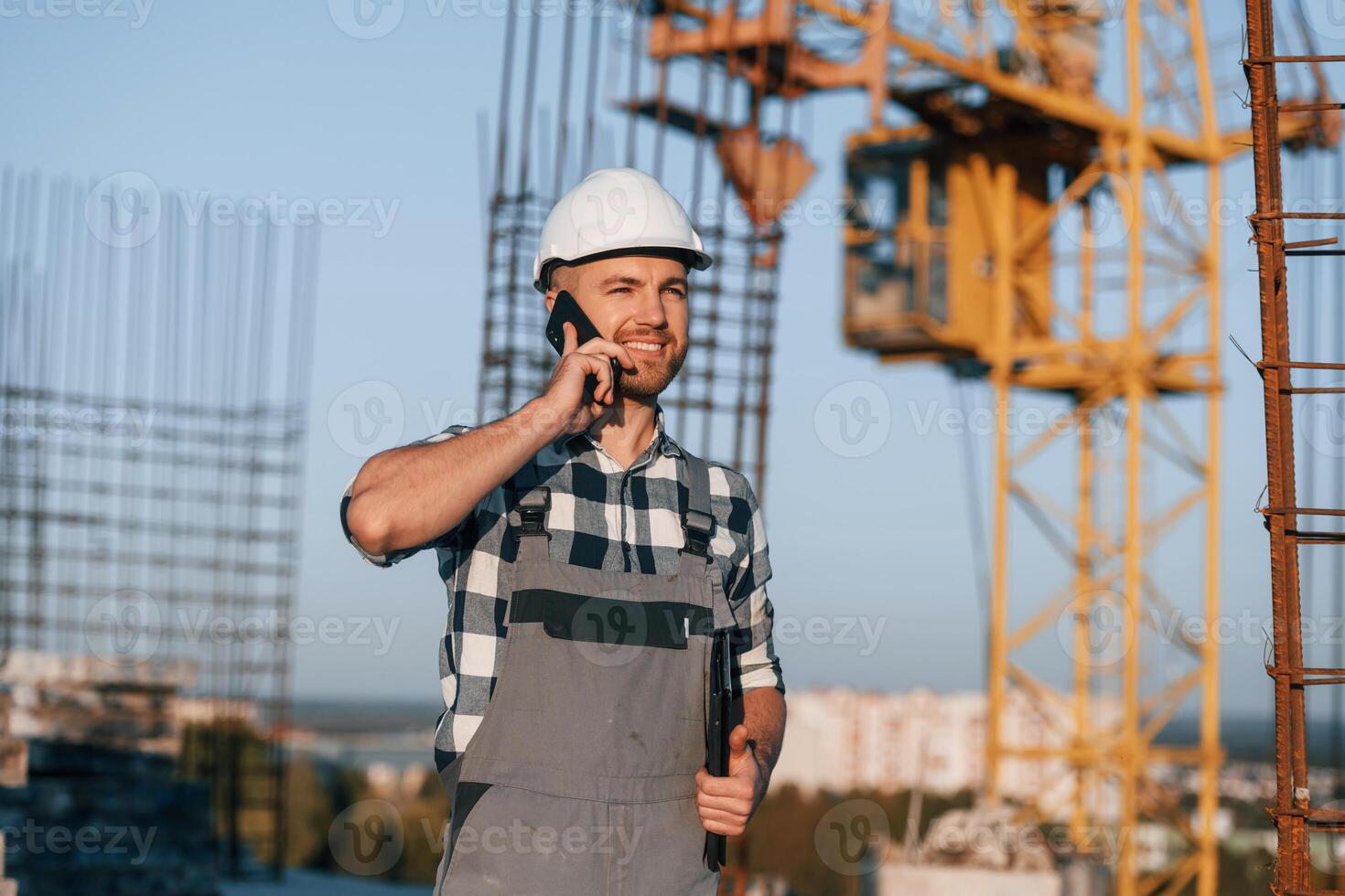 Beautiful man is working on the construction site at daytime and talking by phone photo