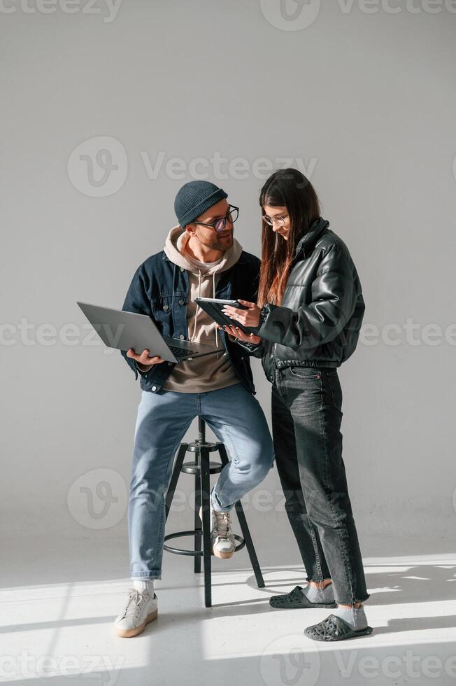 Beautiful man ,and woman are together in the studio against background. With laptop and tablet in hands photo