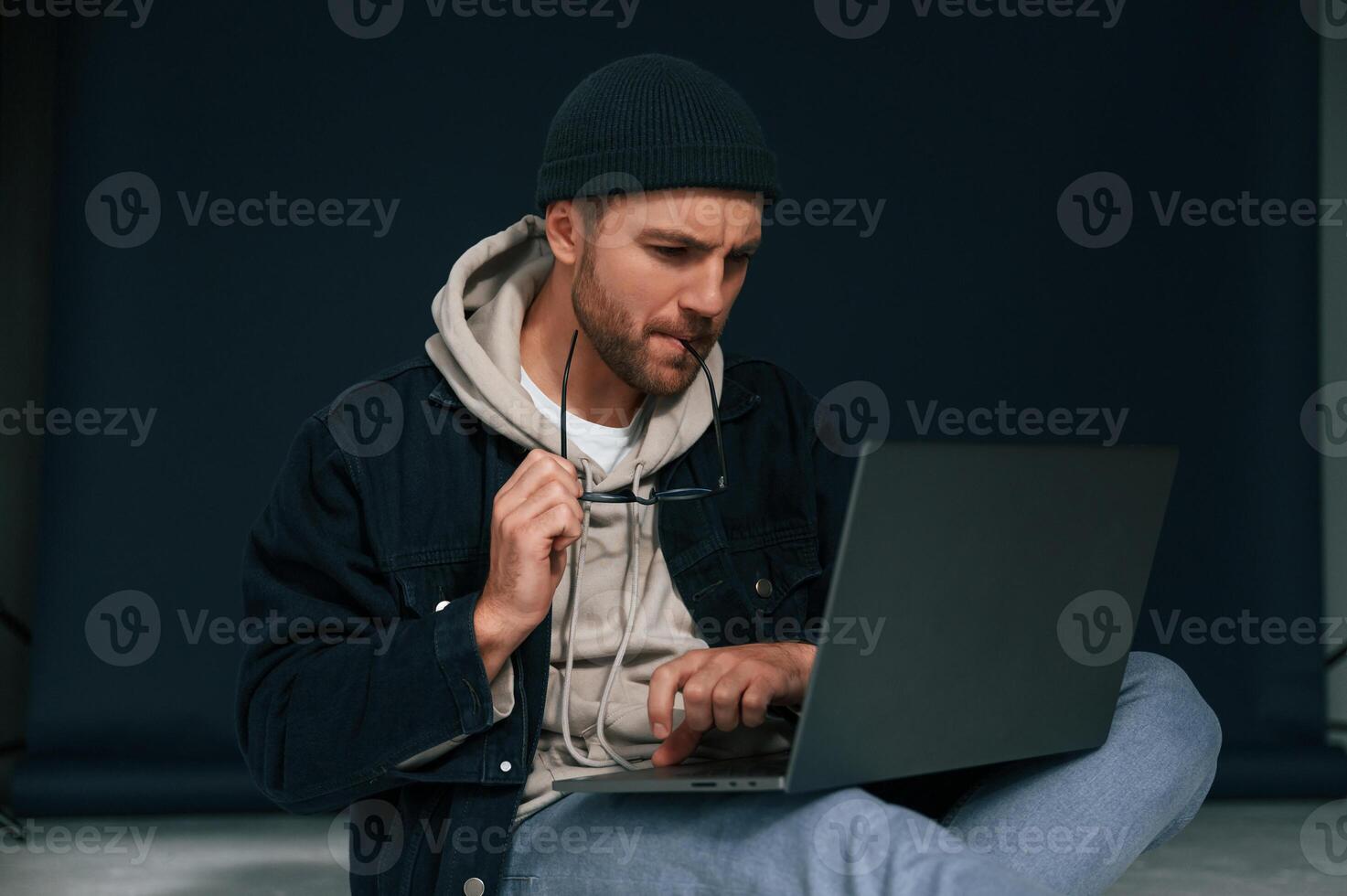 Sitting and using laptop. Handsome man is in the studio against background photo