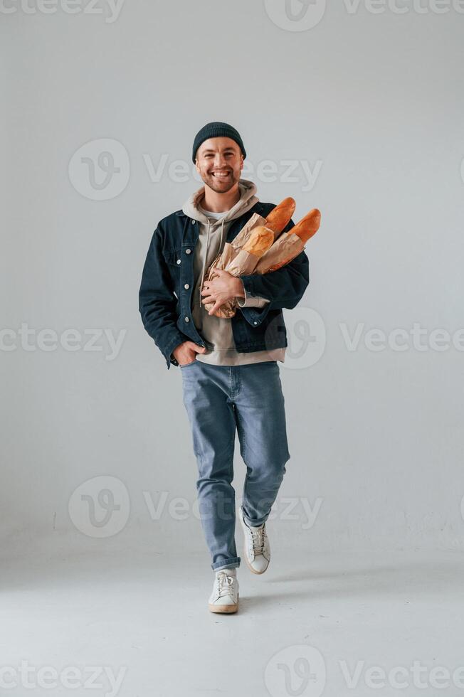 Guy is ,walking and holding baguettes. Handsome man is in the studio against white background photo