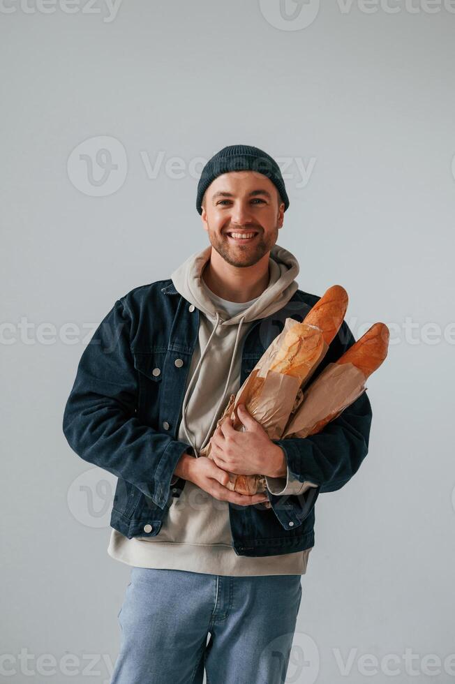 Man in hat is holding baguettes. Guy is in the,, studio against white background photo