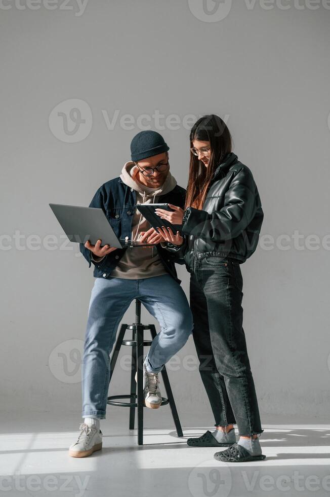 Beautiful ,man and woman are together in the studio against background. With laptop and tablet in hands photo