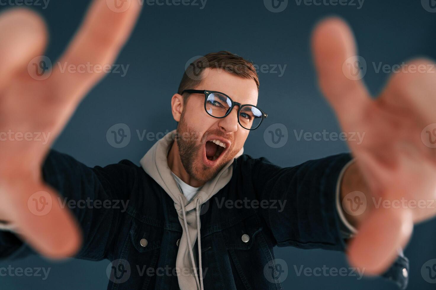 Guy i,s pretending that he's doing photoshoot by using hands gestures. Handsome man is in the studio against blue background photo