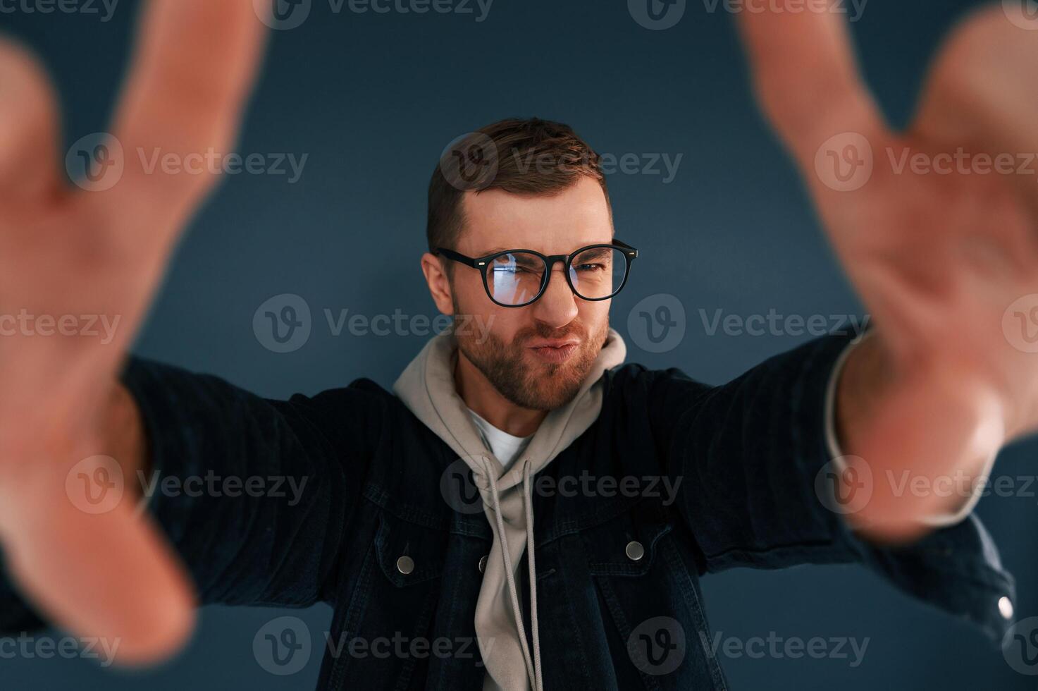 Guy is, pretending that he's doing photoshoot by using hands gestures. Handsome man is in the studio against blue background photo