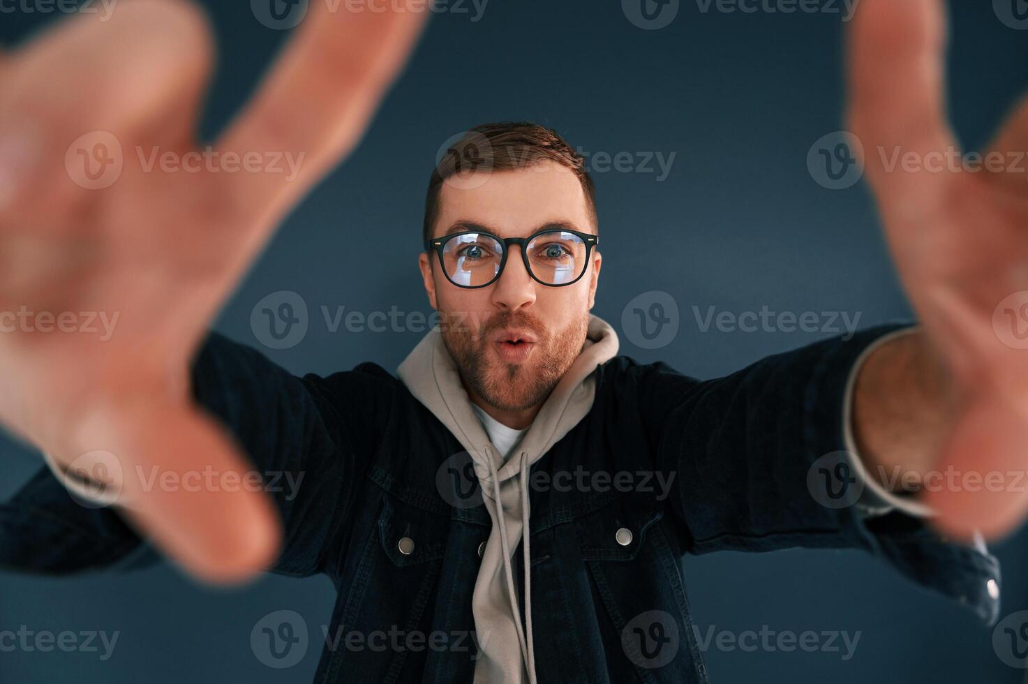Guy,, is pretending that he's doing photoshoot by using hands gestures. Handsome man is in the studio against blue background photo