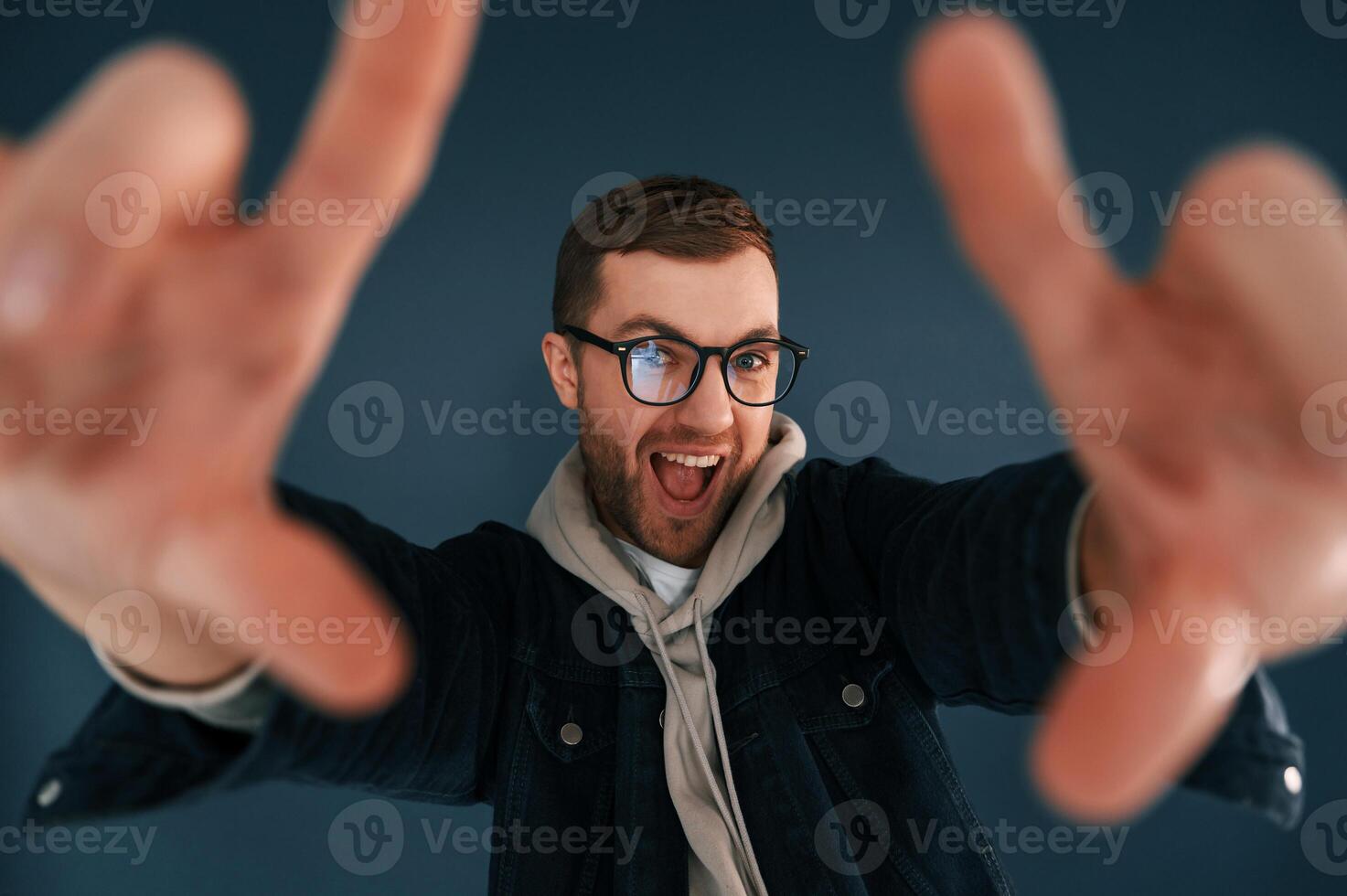 Guy is pretending, that he's doing photoshoot by using hands gestures. Handsome man is in the studio against blue background photo
