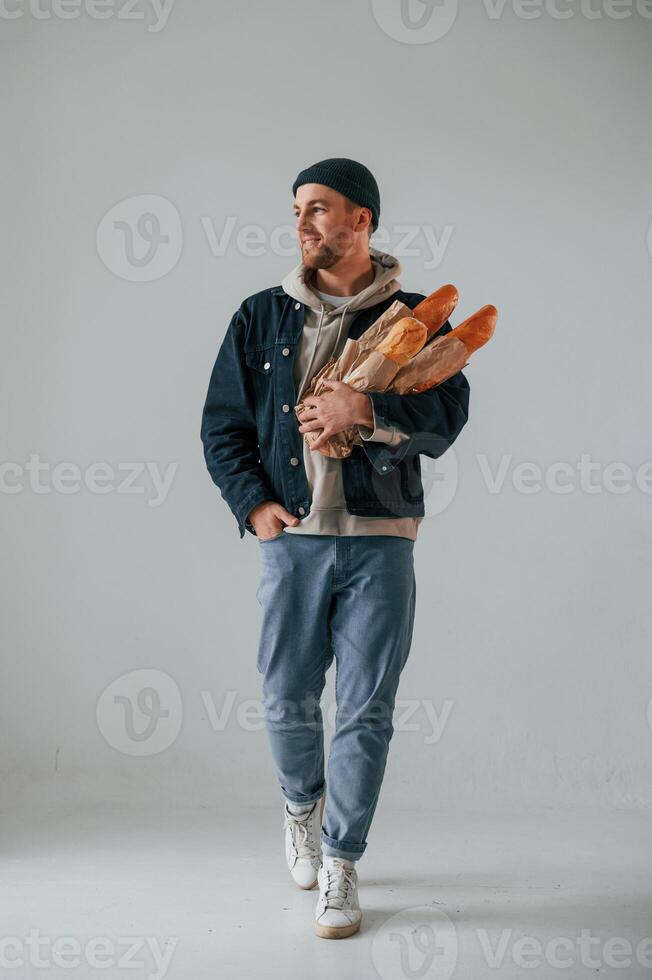 Man in hat is holding baguettes. Guy is in the studio against white background photo