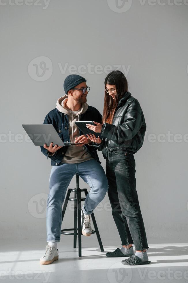 Beautiful man and woman, are together in the studio against background. With laptop and tablet in hands photo