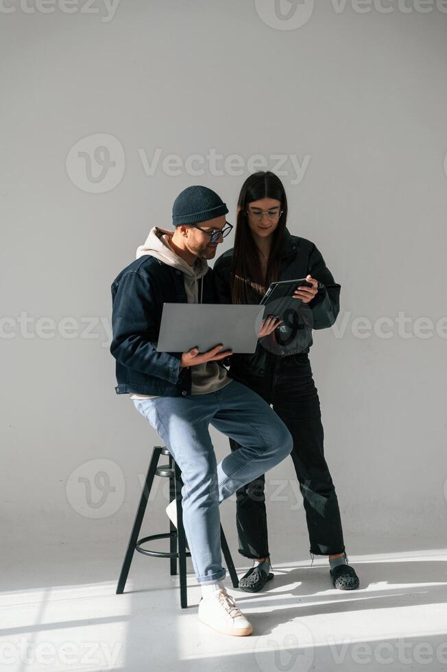 Beautiful man, and woman are together in the studio against background. With laptop and tablet in hands photo