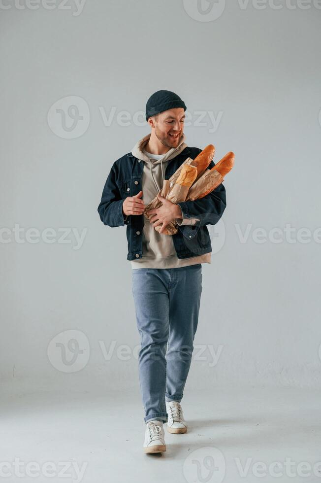 Guy is walking and holding baguettes. Handsome man is in the studio against white background photo