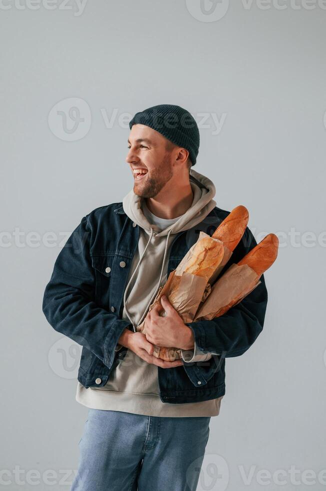 Man in hat is holding baguettes. Guy, is in the studio against white background photo