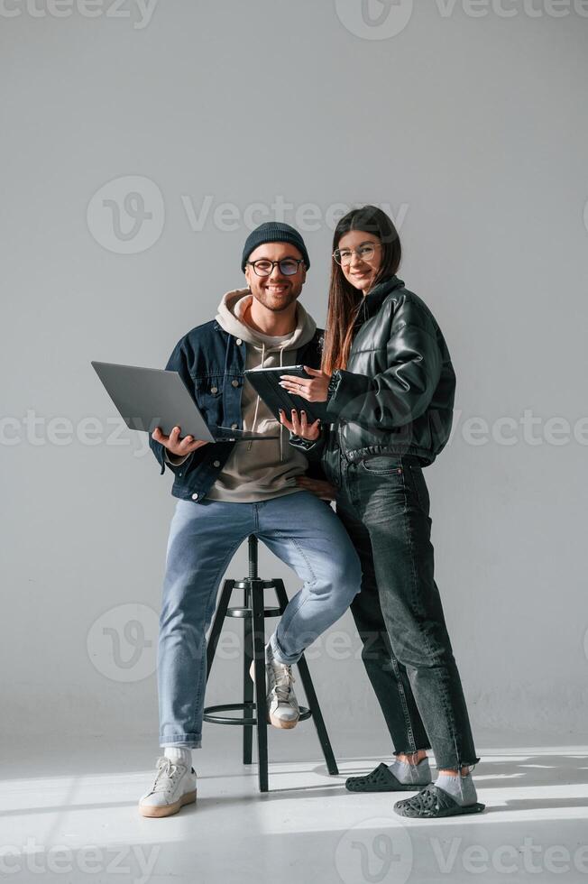 Beautiful ,,man and woman are together in the studio against background. With laptop and tablet in hands photo