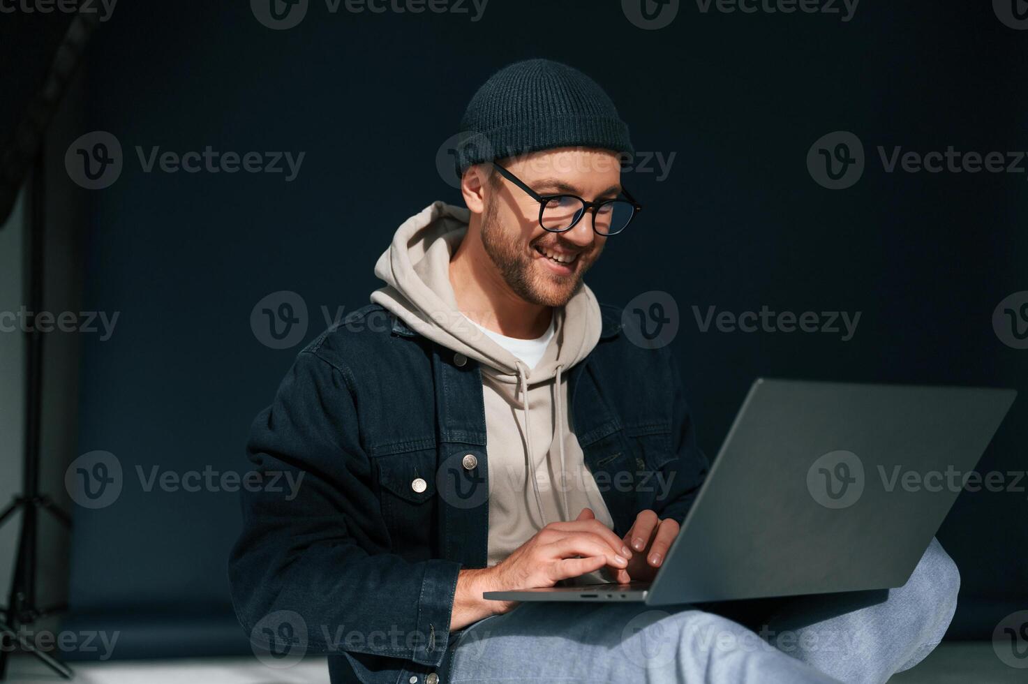 Using laptop and smiling. Handsome man is in the studio against background photo