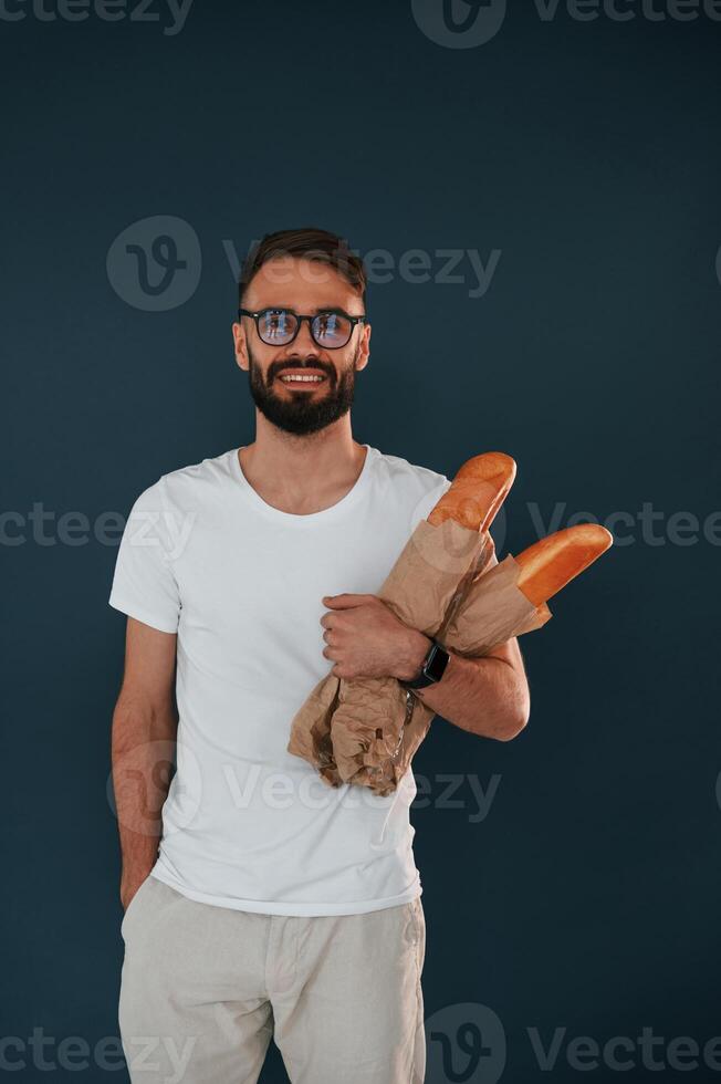 With, baguettes in hand. Handsome man is in the studio against blue background photo