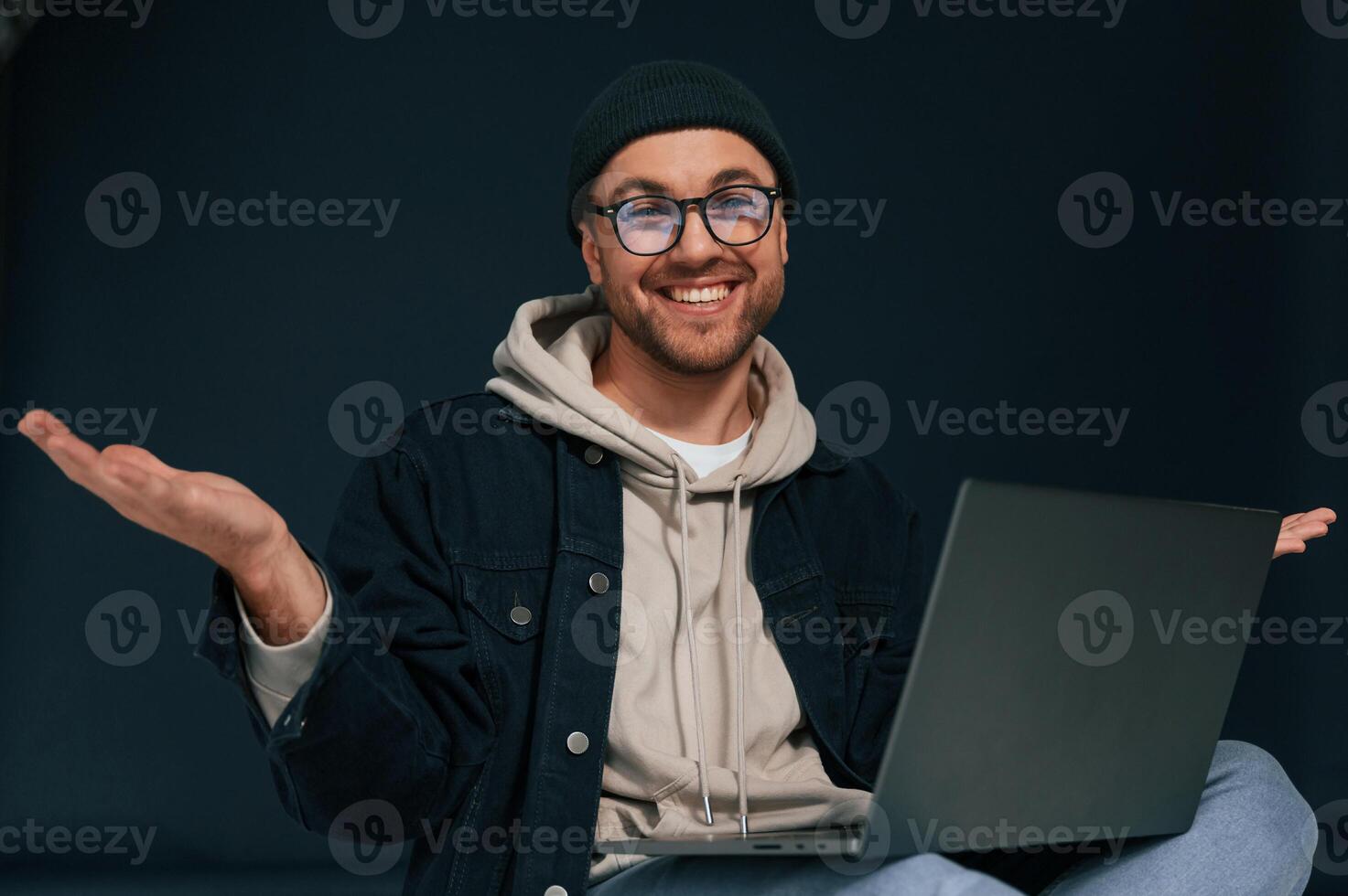 Smiling, sitting and using laptop. Handsome man is in the studio against background photo