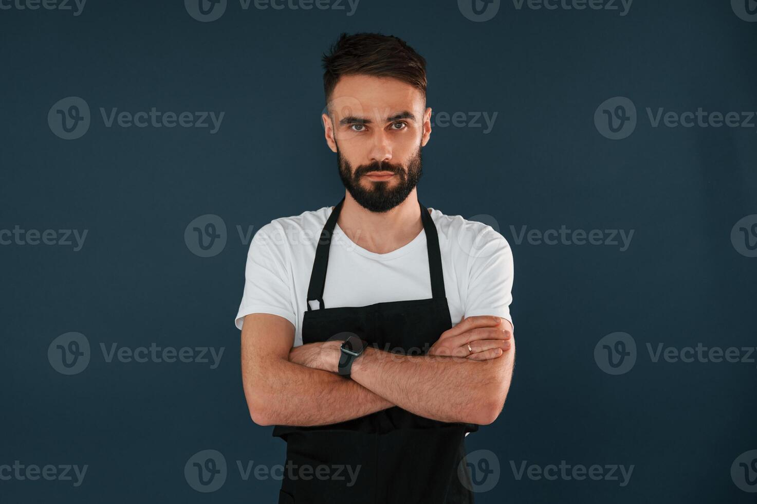 Cafe worker is in apron. Handsome man is in the studio against blue background photo