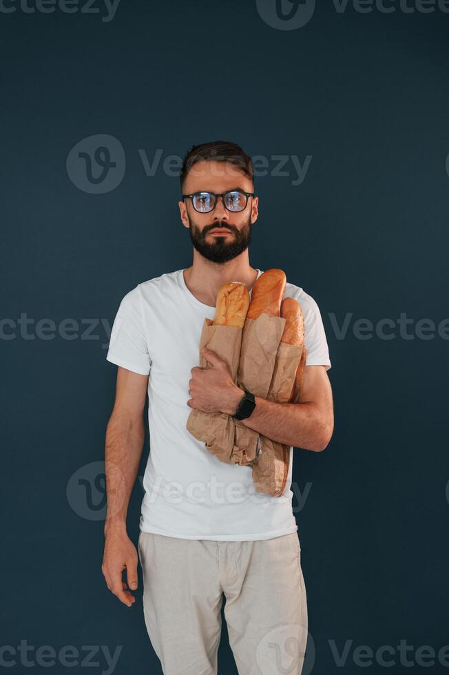 With baguettes in hand. Handsome man is in the studio against blue background photo