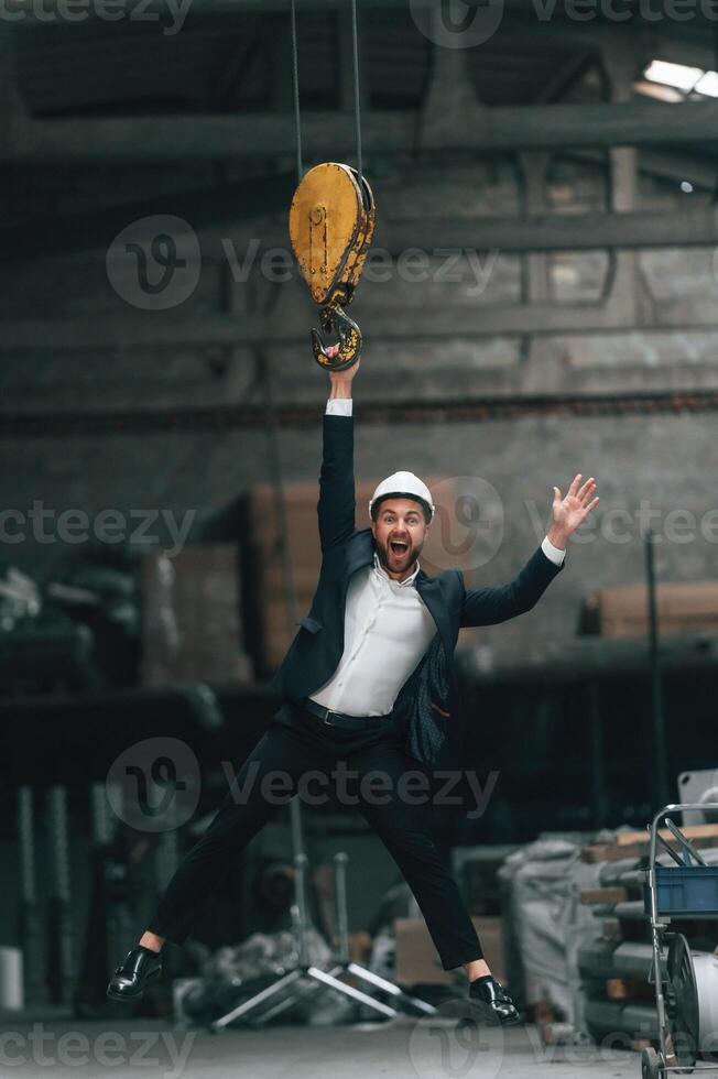 Hanging on the crane hook. Manager in ,black, formal wear at the factory photo