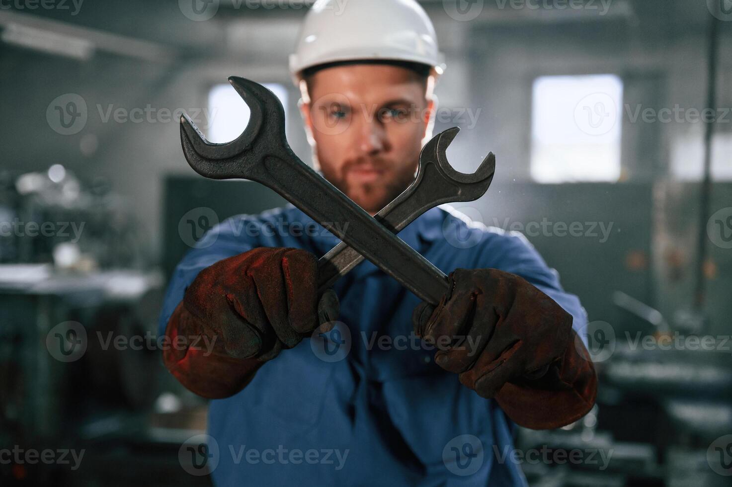 Holding ,two wrenches.. Factory worker in blue uniform is indoors photo
