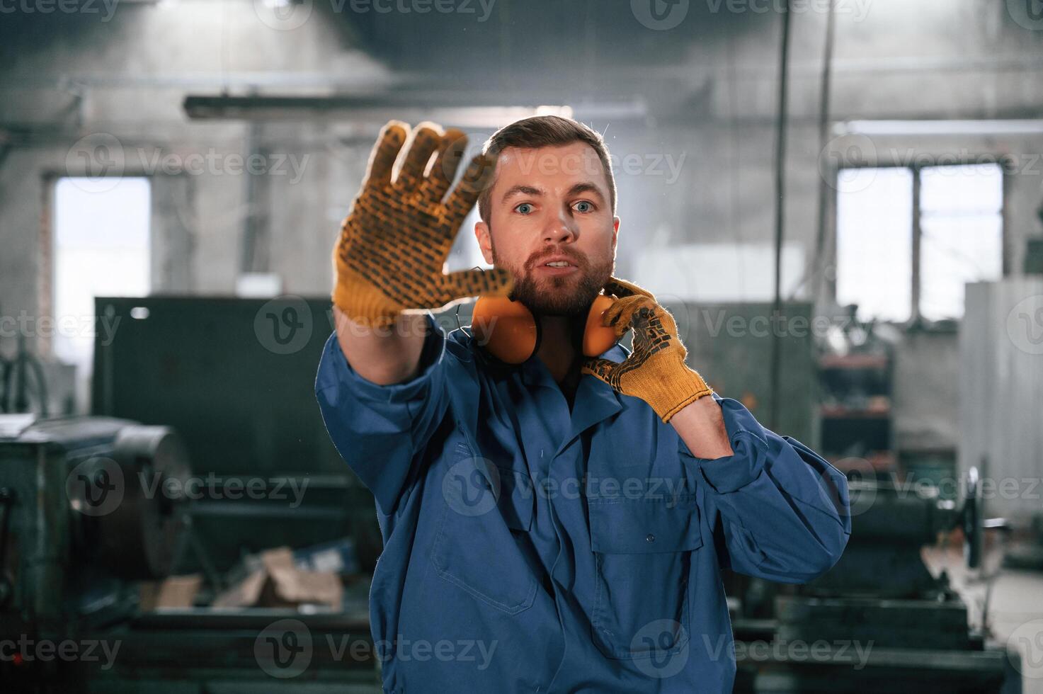 Showing stop gesture by a hand. Factory ,worker, in blue uniform is indoors photo