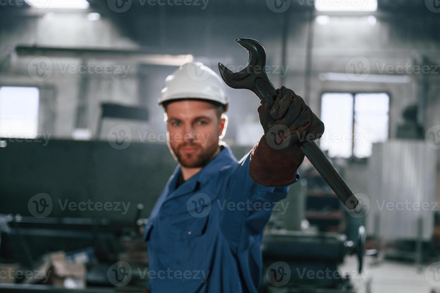 Wrench, in the hand. Factory worker in blue uniform is indoors photo