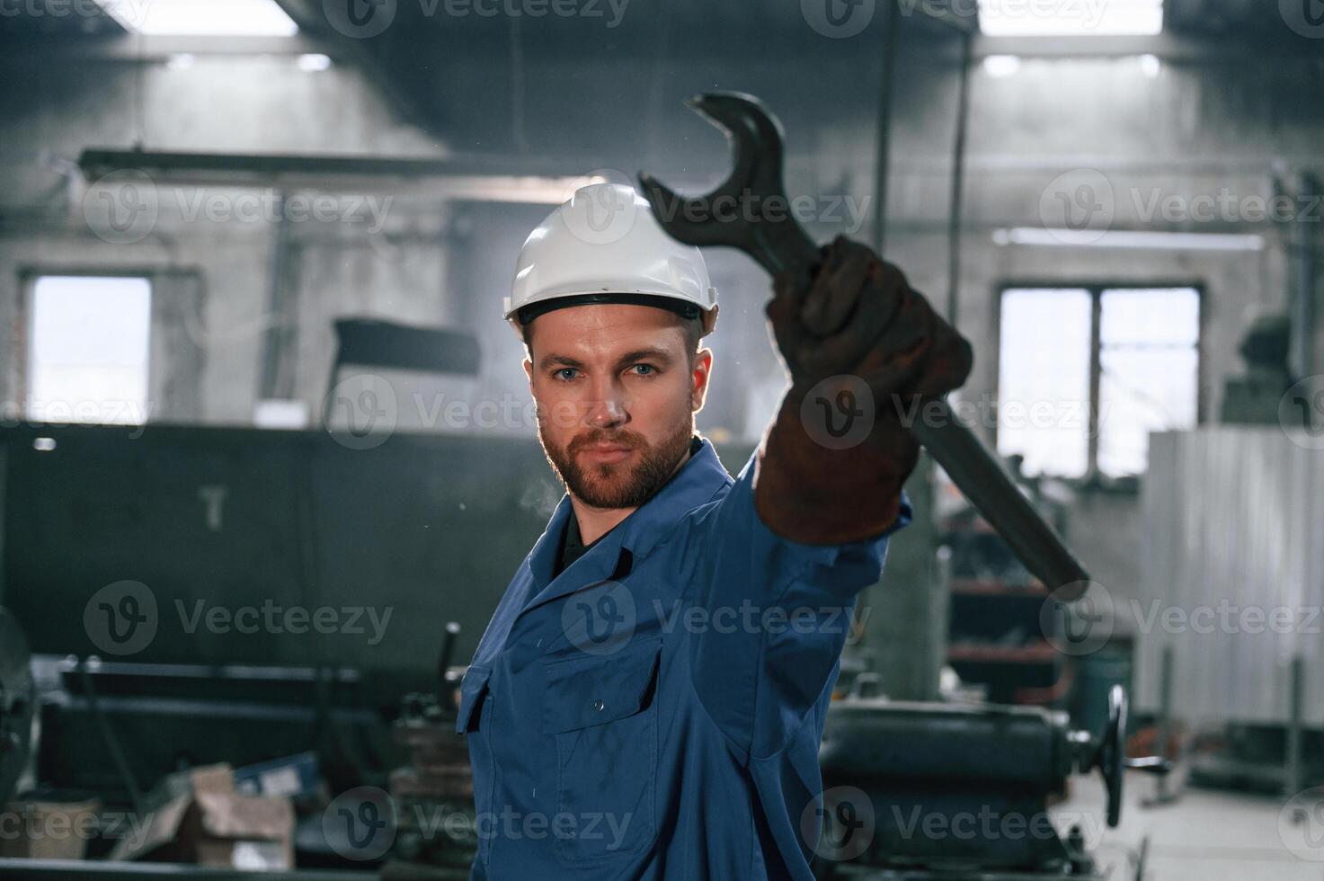 Wrench i,n the hand.. Factory worker in blue uniform is indoors photo