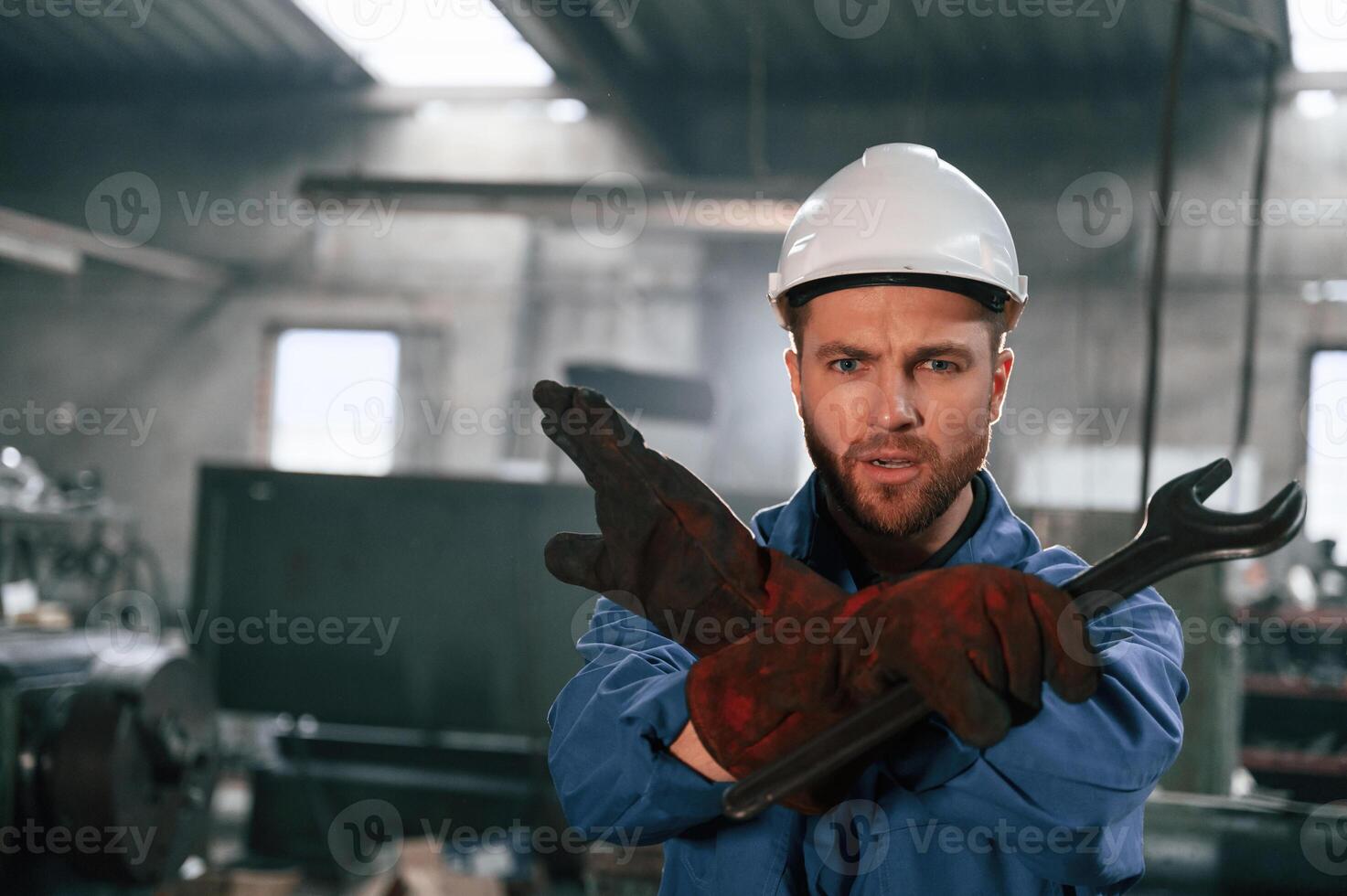 Hands gesture. With wrench. Factory worker in blue uniform is indoors photo