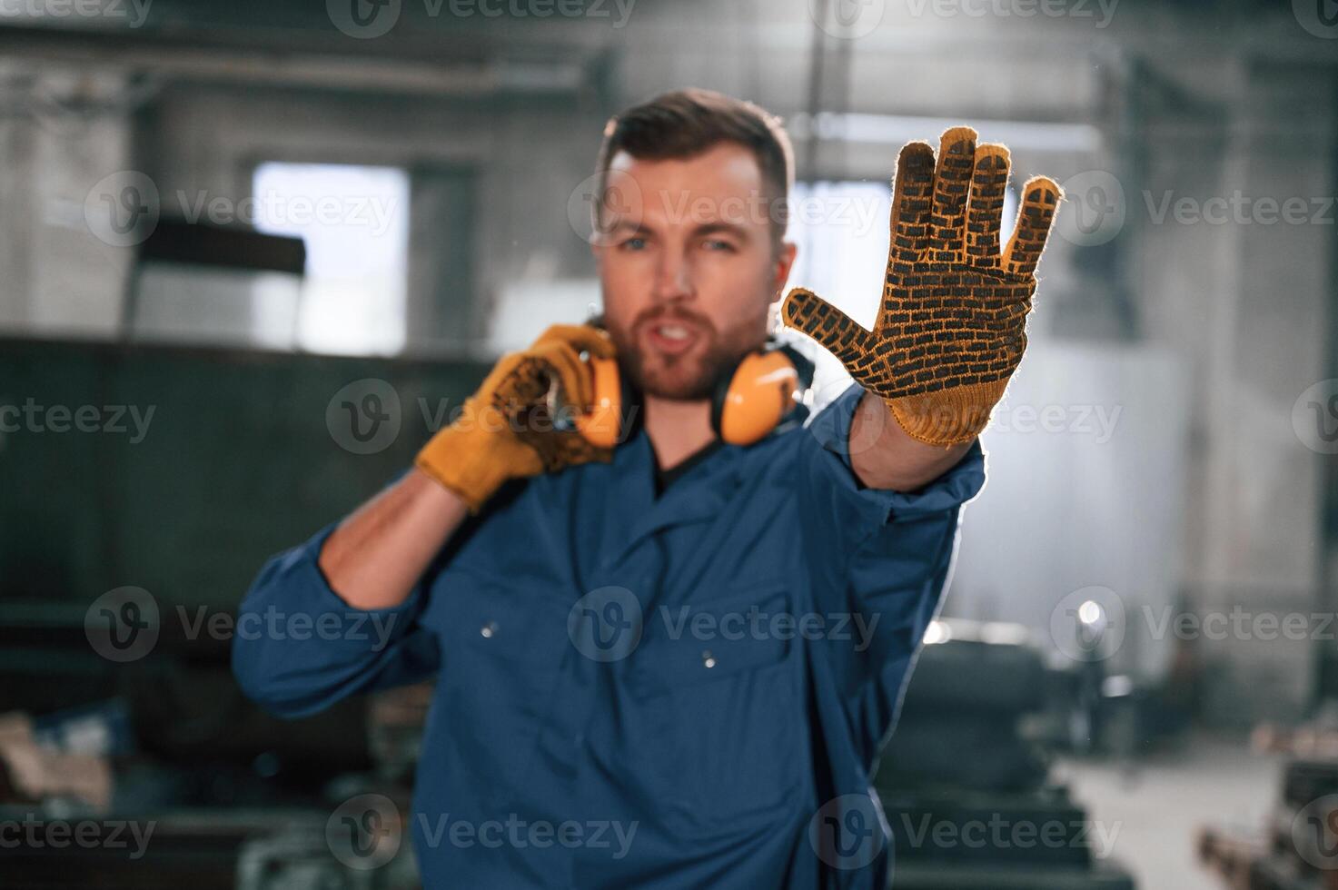 Showing stop gesture, by a hand. Factory worker in blue uniform is indoors photo