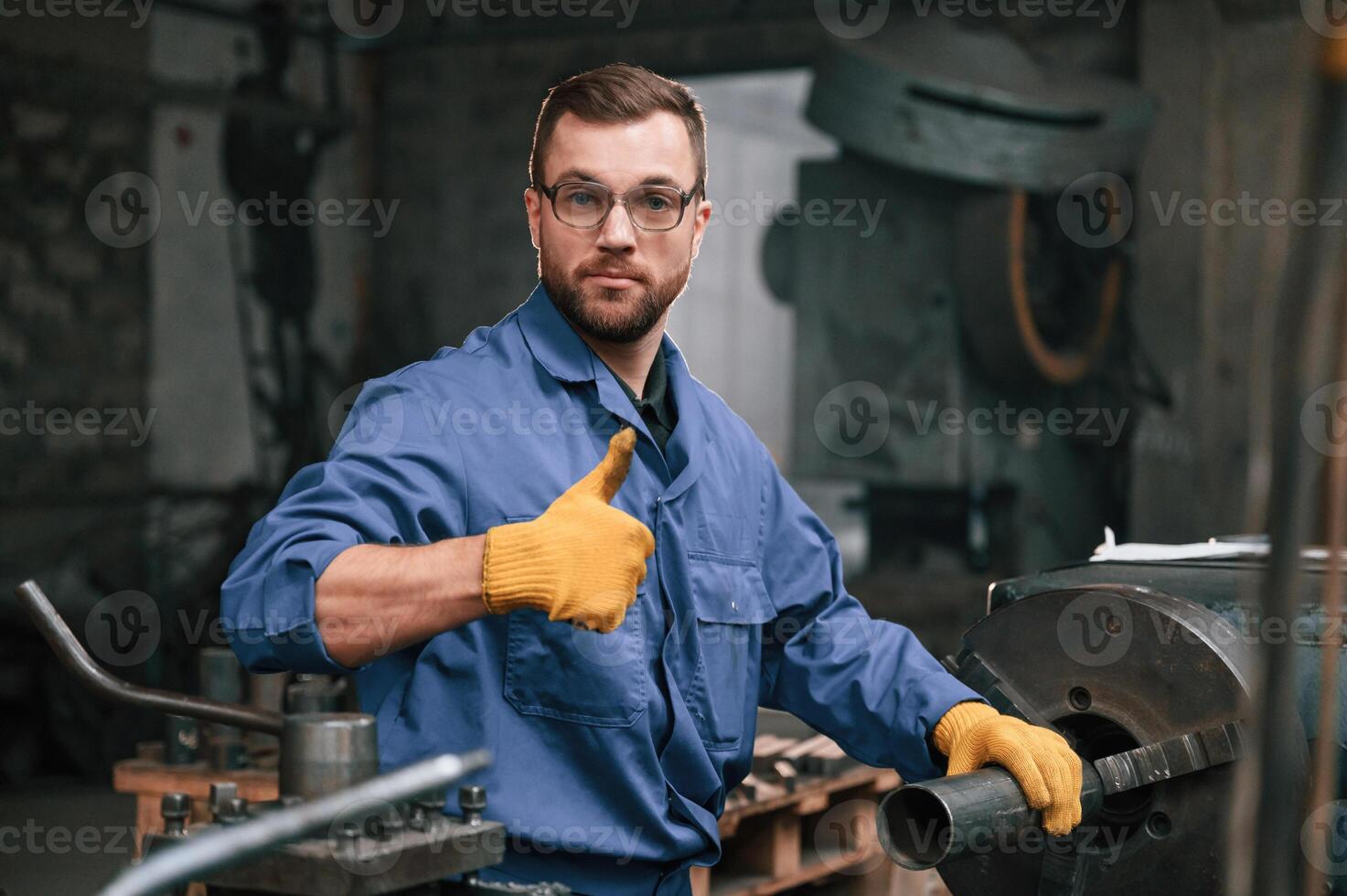 Job ,is done. Showing thumb up. Factory worker in blue uniform is indoors photo