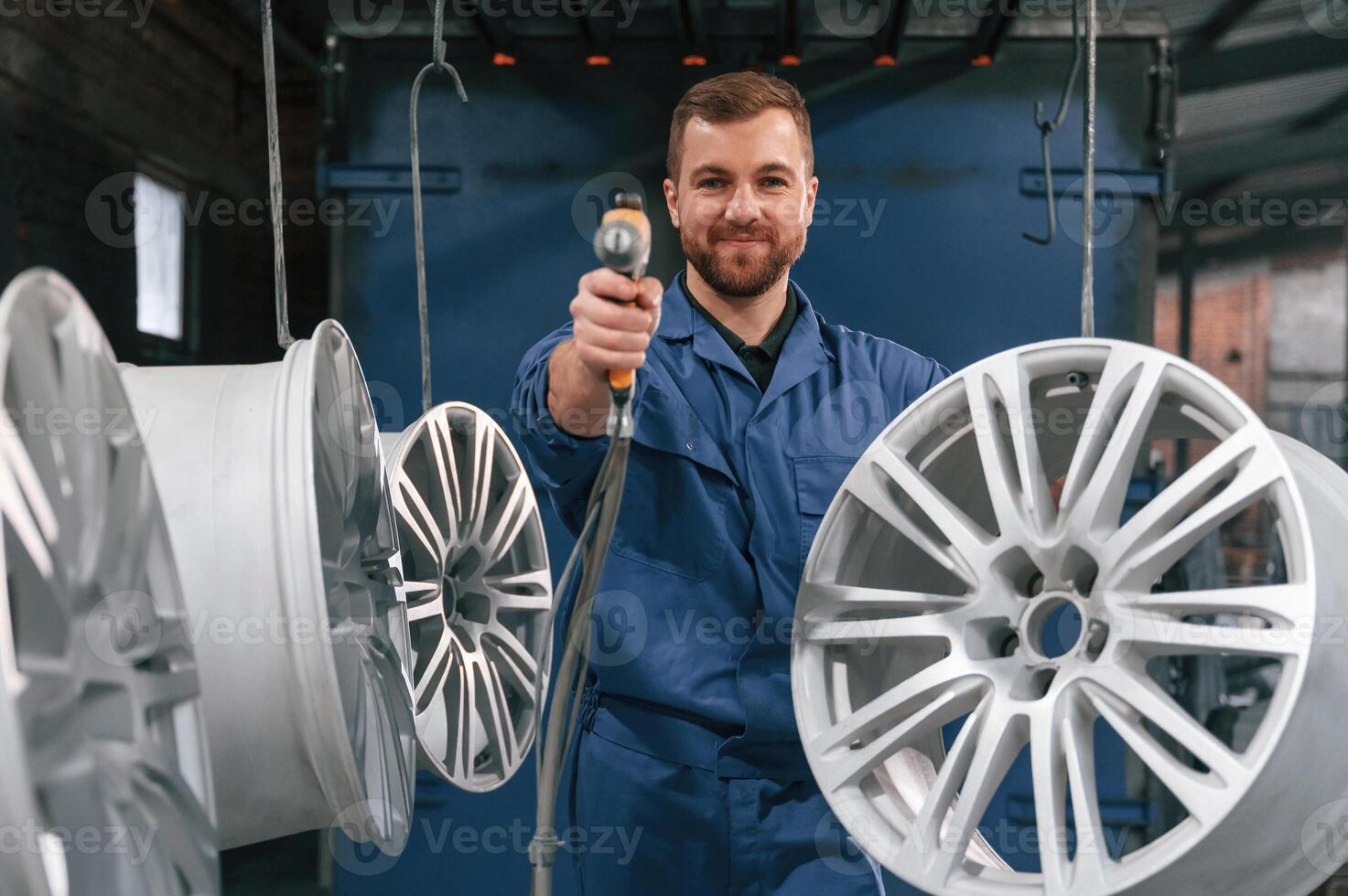 Holding paint, spray gun. Car service station, worker is taking care about disks of tires photo