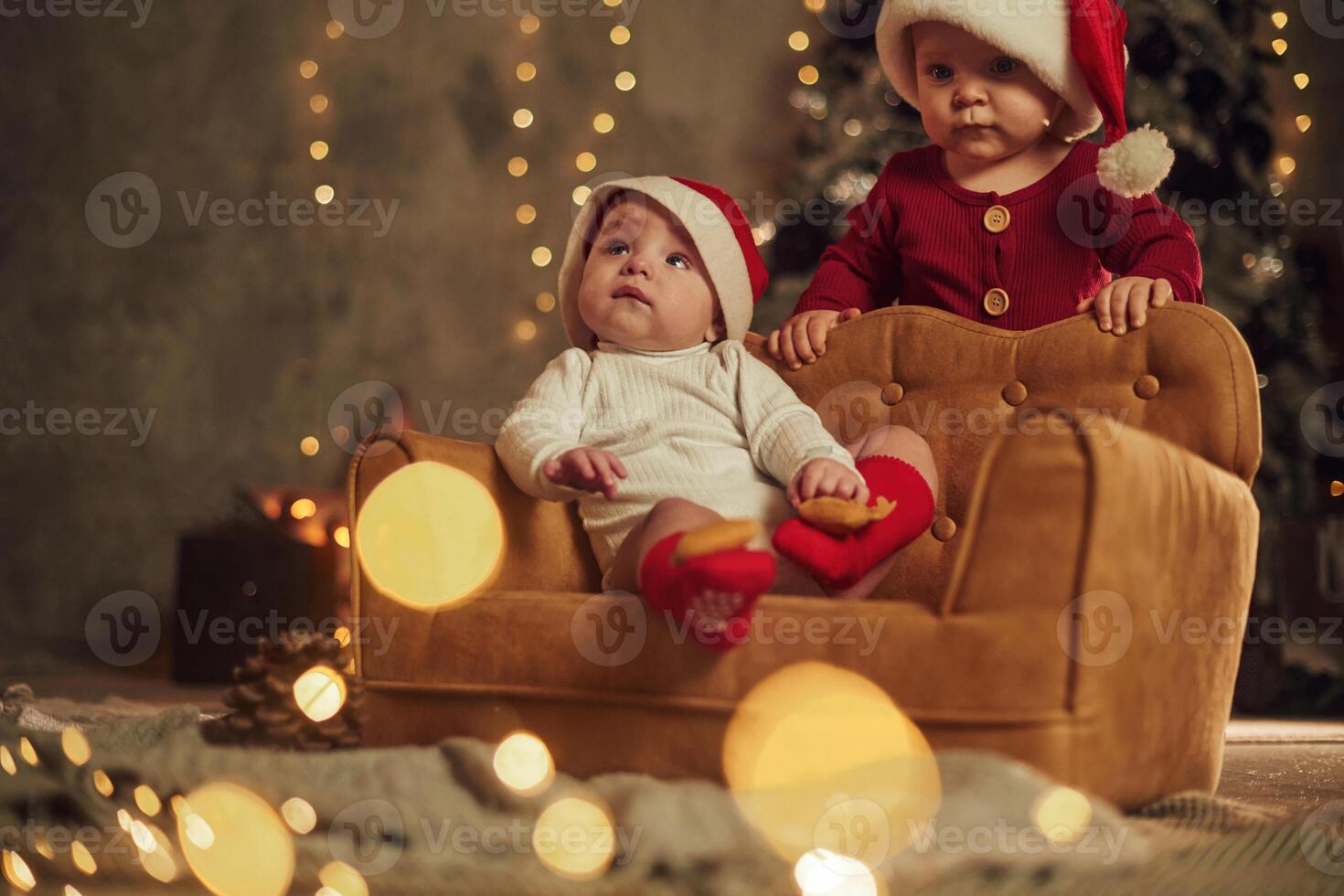 Two little kids in Santa hats, are celebrating holidays indoors together photo