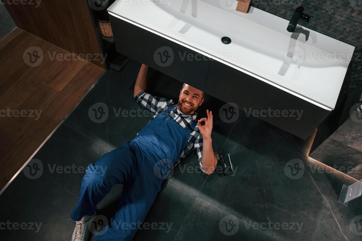 Job, is done. Lying down on the floor. Plumber in blue uniform is at work in the bathroom photo