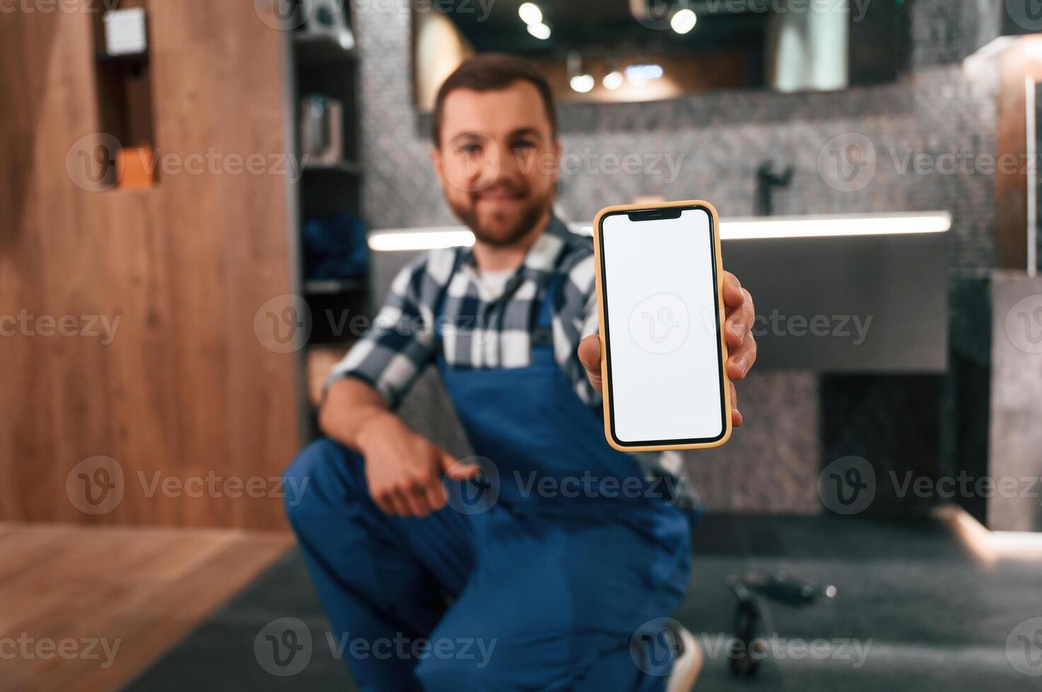 Holding smartphone.. Plumber in blue uniform is at work in the bathroom photo
