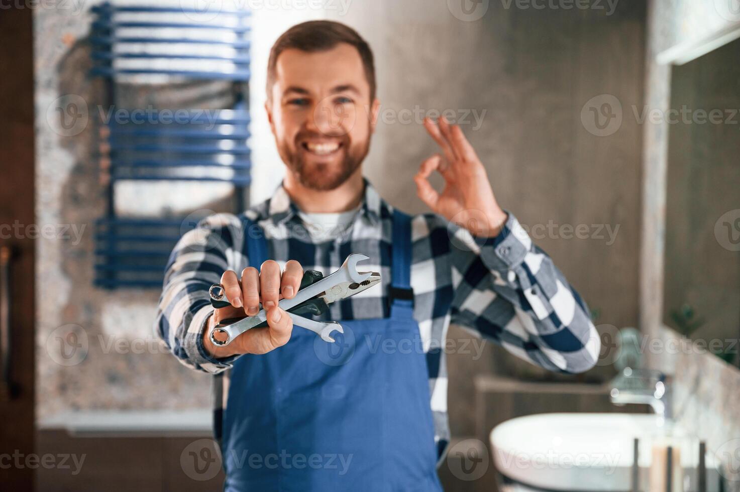 Holding wrenches. Plumber, in blue uniform is at work in the bathroom photo