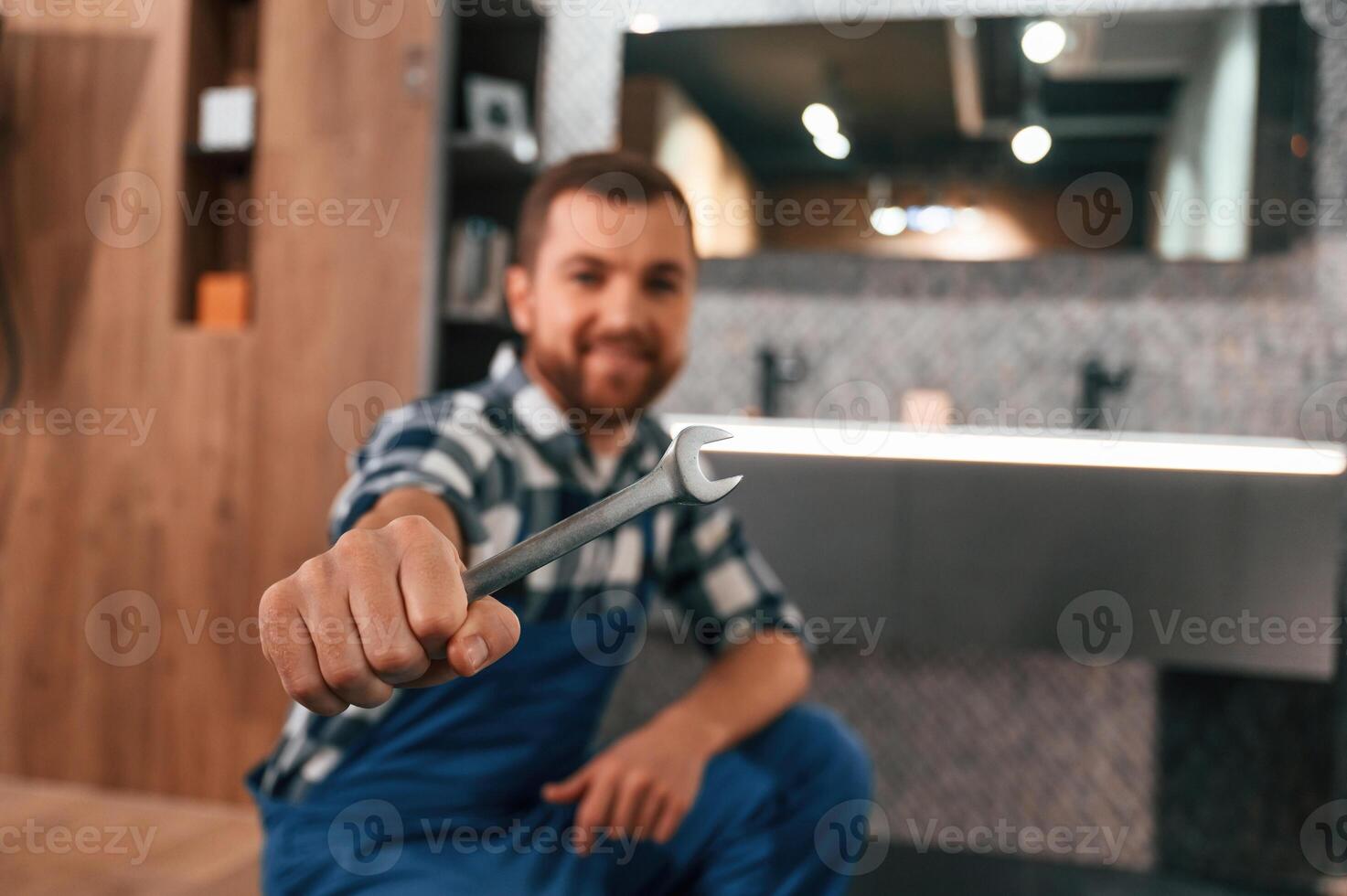 With wrench in hand. Plumber,, in blue uniform is at work in the bathroom photo