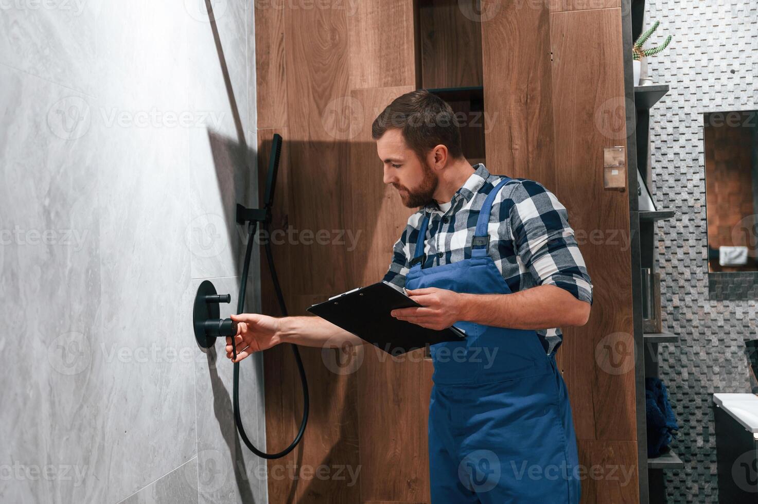 Repairs the shower faucet. Plumber in blue uniform is at work in the bathroom photo