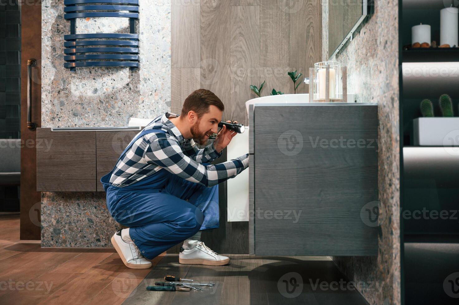 Plumber in blue uniform is at work in the bathroom photo