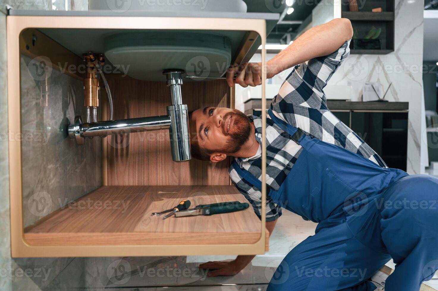 Busy ,by ,repairing siphon. Plumber in blue uniform is at work in the bathroom photo