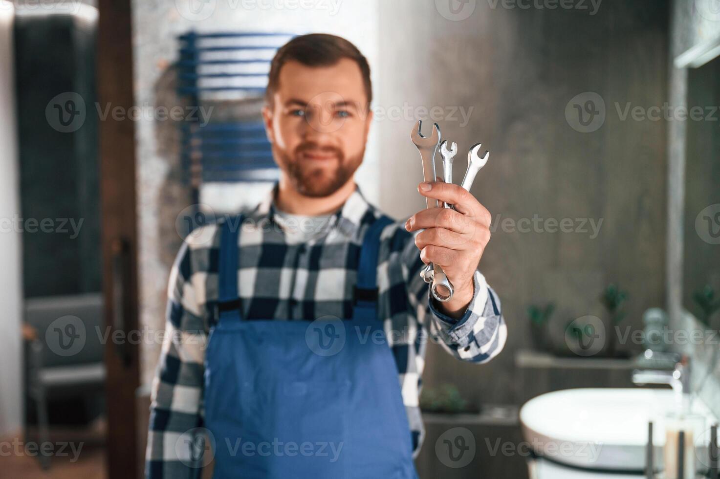 Holding wrenches. Plumber in blue uniform is at work in the bathroom photo