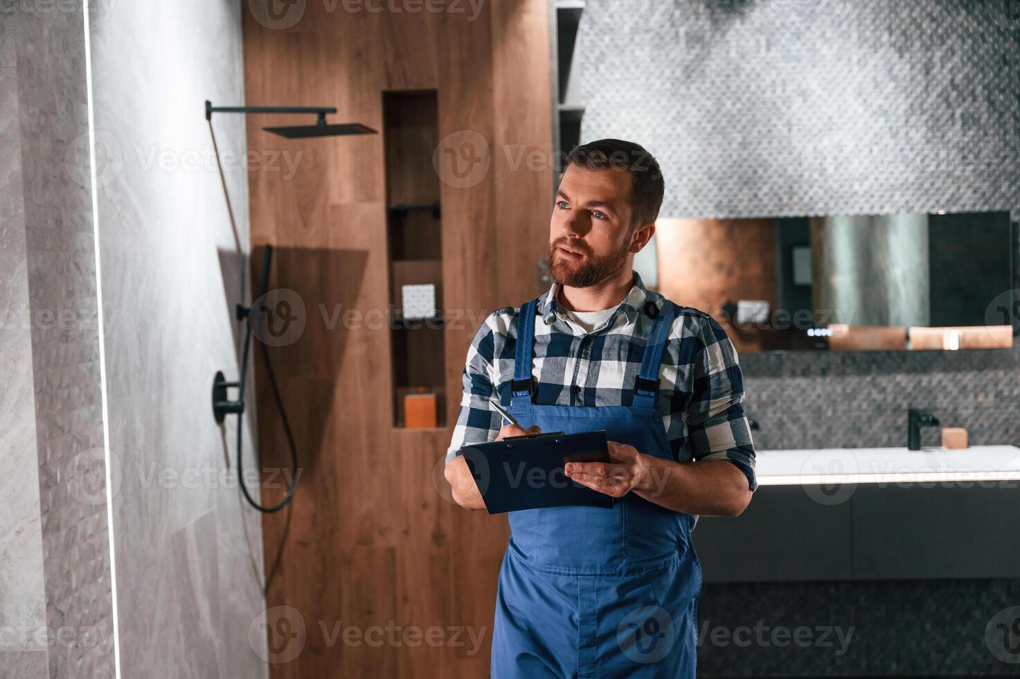 Writes, down i,nformation in a notebook. Plumber in blue uniform is at work in the bathroom photo