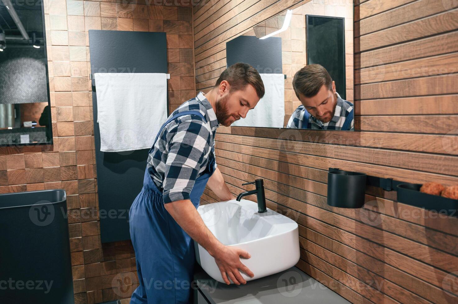 Holding and moving a sink. Plumbe,r in blue uniform is at work in the bathroom photo