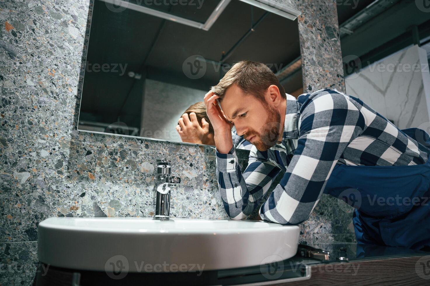 Can't fix the crane. Plumber in ,blue uniform is at work in the bathroom photo