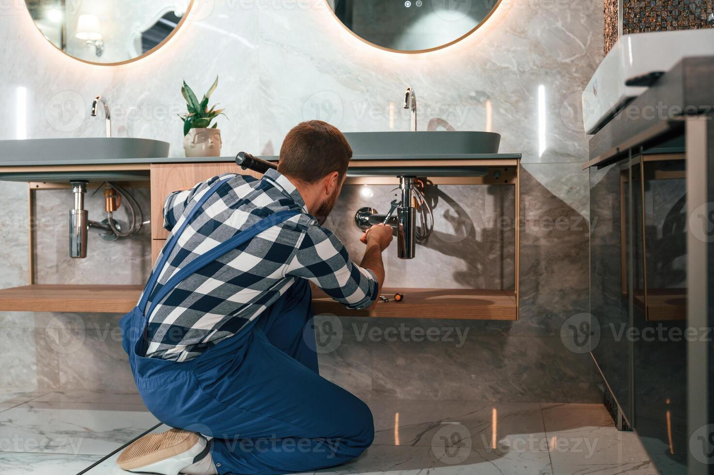 Busy ,by repairing siphon. Plumber in blue uniform is at work in the bathroom photo