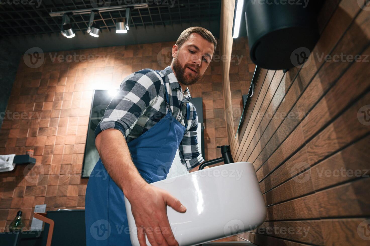 Holding and moving a sink. Plumber in blue uniform is at work in the bathroom photo