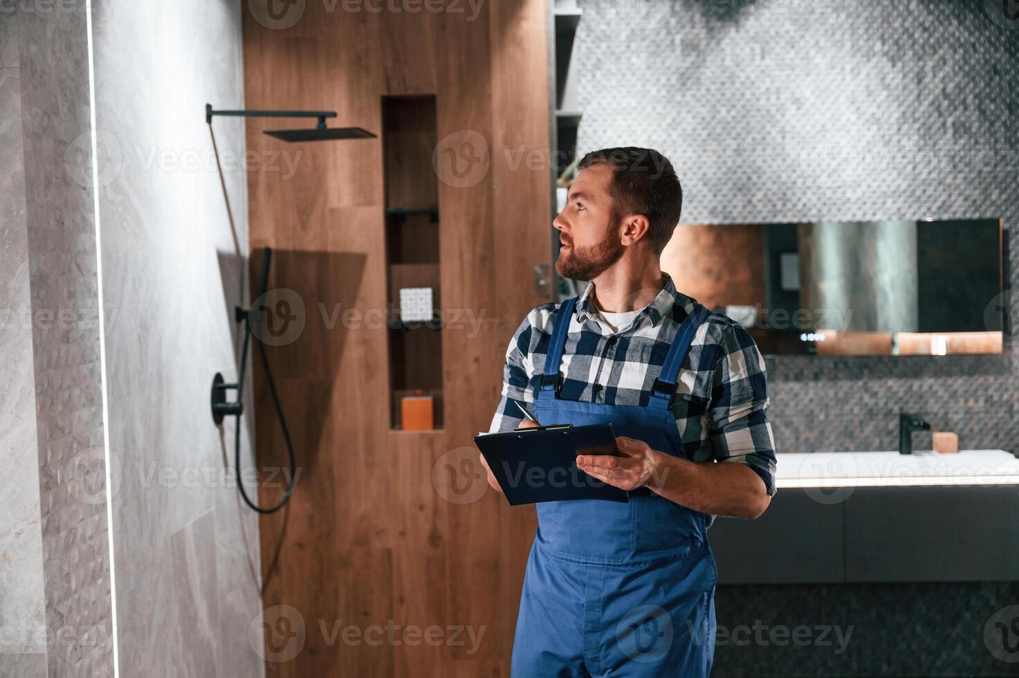 Writes down, information in a notebook.. Plumber in blue uniform is at work in the bathroom photo