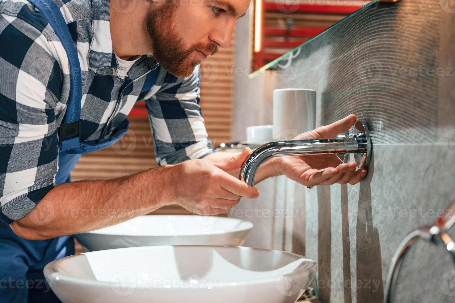 Close up view. Fixing water, tap. Plumber in blue uniform is at work in the bathroom photo