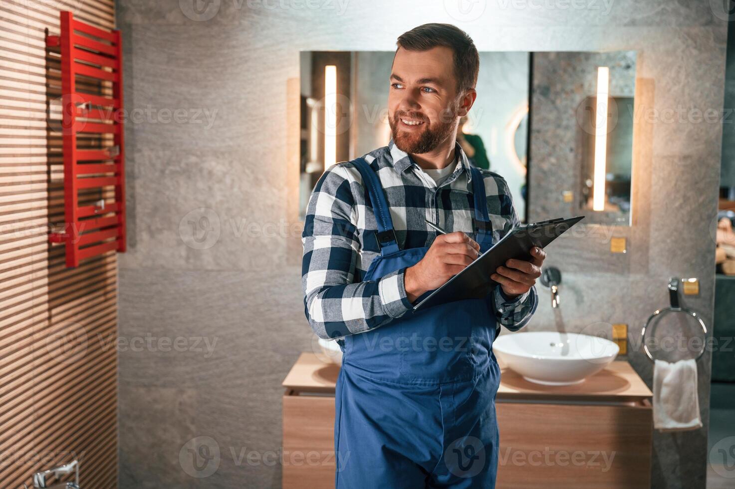 With ,notepad in, hands. Plumber in blue uniform is at work in the bathroom photo