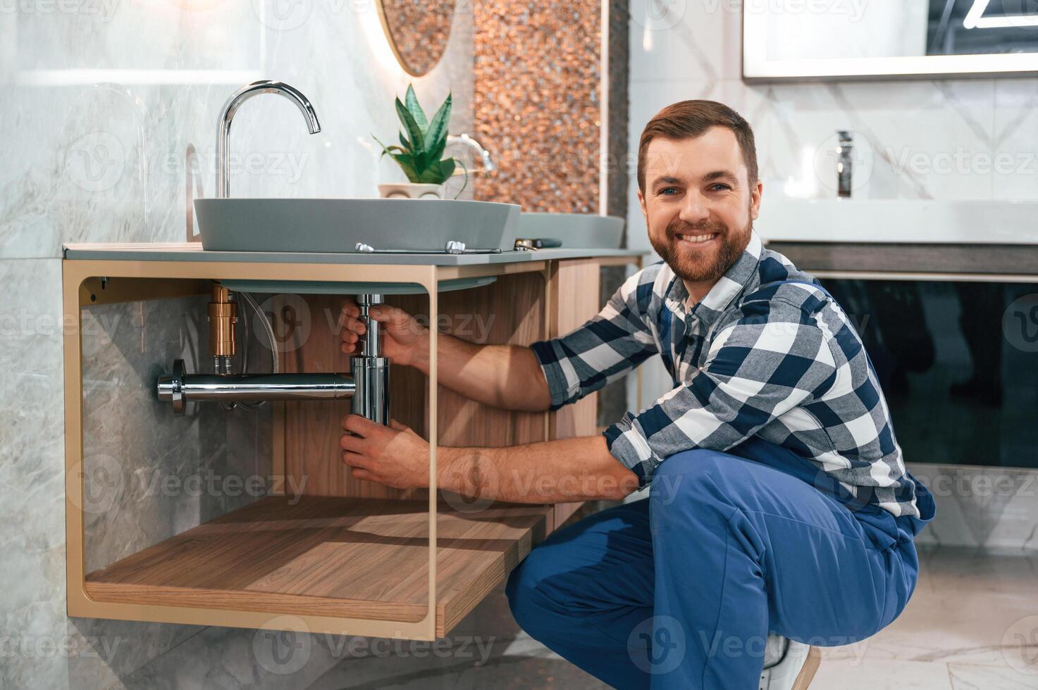 Positive plumber in blue uniform, is at work in the bathroom photo